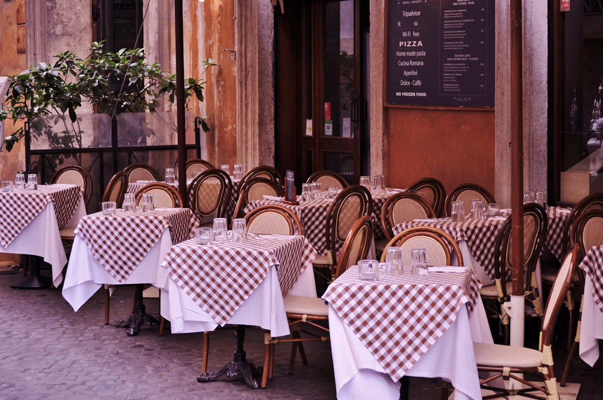 A narrow Naples street at dusk with the warm glow of a pizzeria entrance and a queue of people waiting outside